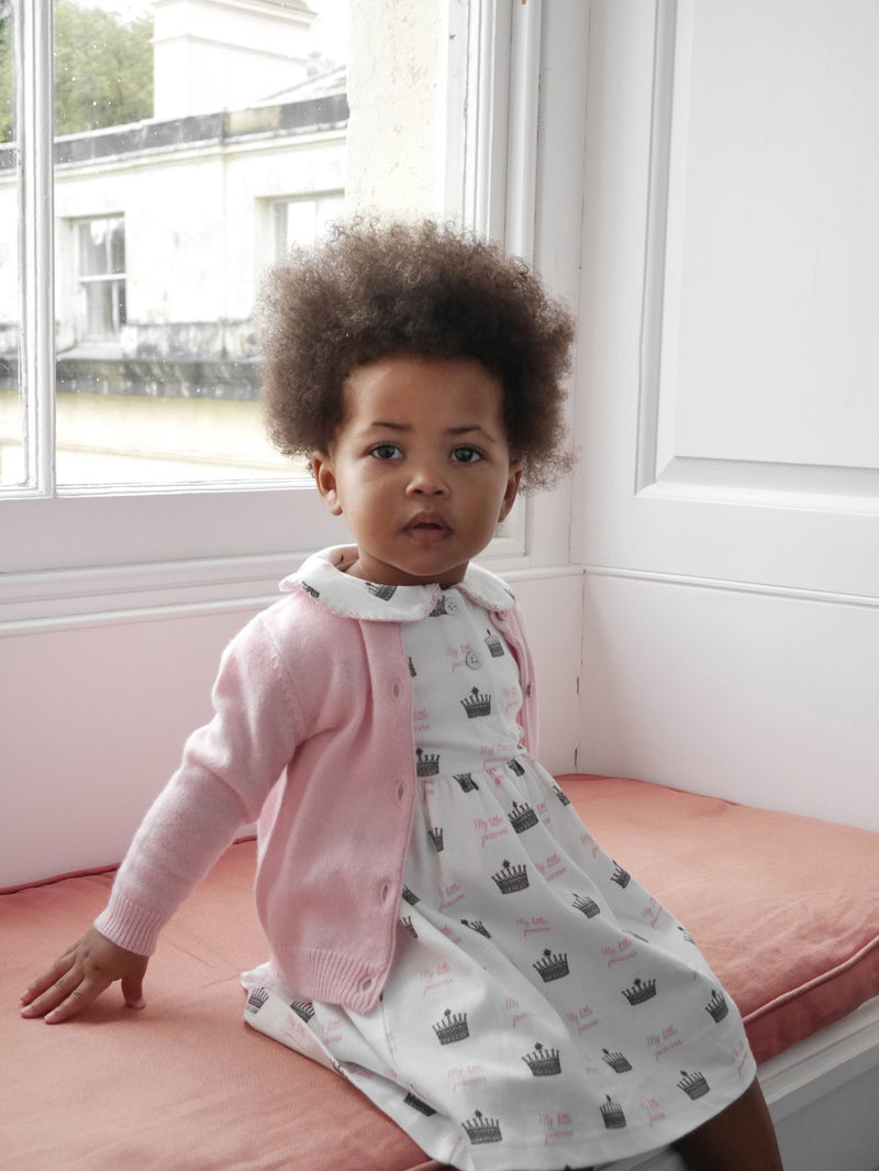 Baby girl wearing princess crown print jersey dress styled with pink cashmere cardigan and hairbow