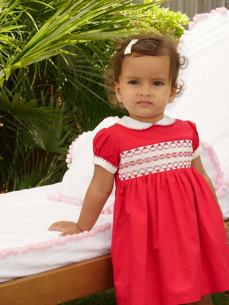 Baby wearing red classic smocked dress, styles with matching hairbow and slippers.