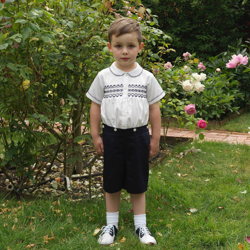 Boy wearing navy smocked, short sleeved shirt and matching navy button on short set