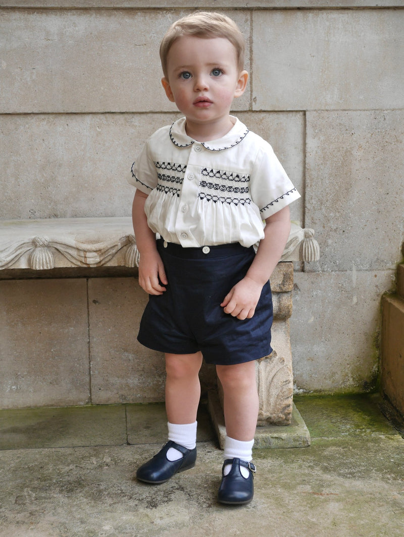 Boy wearing navy smocked, short sleeved shirt and matching navy button on short set