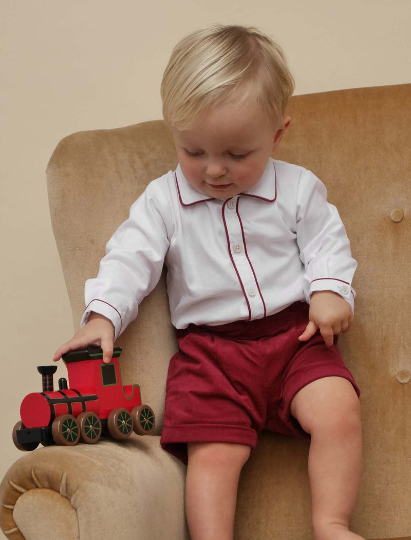 Baby boy wearing burgundy babycord short and white pique shirt set.